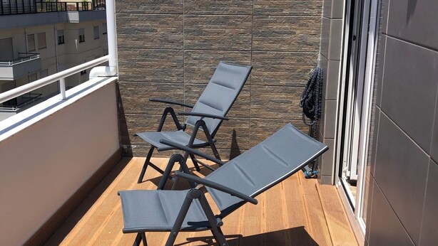 Ein Balkon mit drei Liegestühlen, einer Steinmauer und Blick auf andere Gebäude.