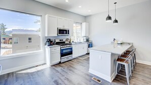 A modern kitchen with white cabinets, a central island with stools, a stove, and a microwave.