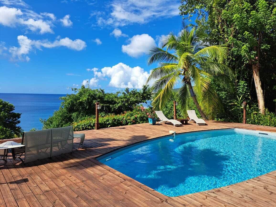 A wooden deck with a swimming pool, lounge chairs, and a view of the ocean.