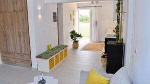A modern living room with a sofa, a coffee table, a plant, and a kitchen area visible through an open door. - Lambisea 2 Bedroom Apartment (Kos)