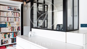 A modern room with a large window, a bookshelf filled with books, and a white desk. - Charming apartment in the heart of Saint-Germain (Paris)