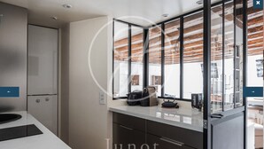 A modern kitchen with a stainless steel refrigerator, a black countertop, and a glass partition. - Charming apartment in the heart of Saint-Germain (Paris)