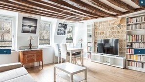 A modern living room with a wooden ceiling, white furniture, a TV, and a bookshelf. - Charming apartment in the heart of Saint-Germain (Paris)