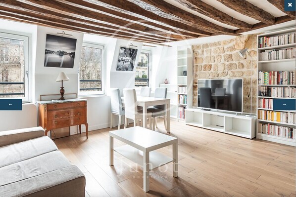A modern living room with a wooden ceiling, white furniture, a TV, and a bookshelf. - Charming apartment in the heart of Saint-Germain (Paris)