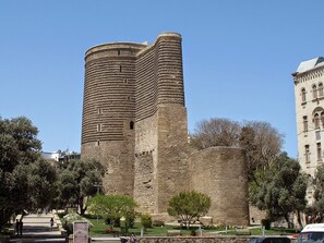 A historic stone tower with a cylindrical shape and crenellations, surrounded by trees and a paved walkway. - MY  MUSIC HOTEL (Bakı)