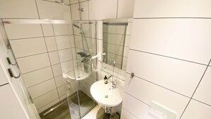 Un baño moderno con ducha envuelta en vidrio, un lavabo blanco y un espejo encima.
