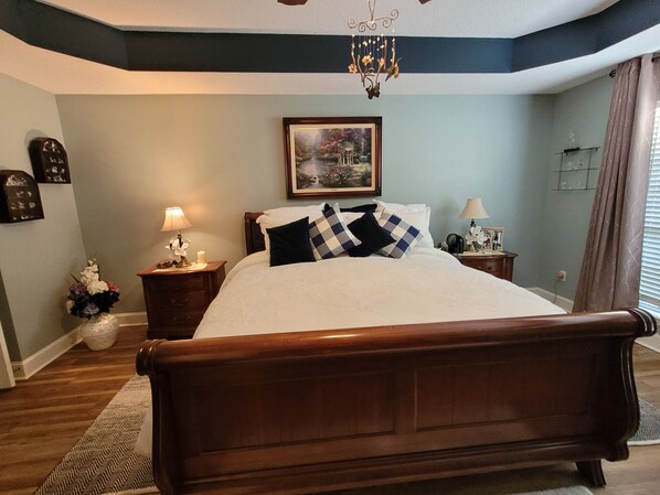 Une chambre à coucher avec un lit en bois, une table de chevet avec une lampe, une horloge murale et un tableau encadré au-dessus du lit.