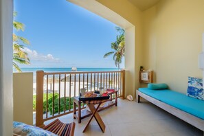 A balcony with a view of the beach, a bed with a blue mattress, and a tray with breakfast items.