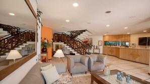 A spacious living area with a sofa, armchairs, a coffee table, and a staircase with wooden railings. - Ilha Flat Hotel (Ilhabela)
