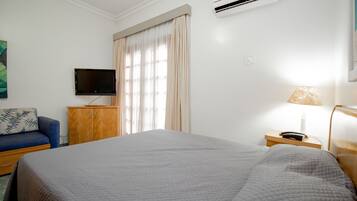 Une chambre d’hôtel avec un grand lit, un téléviseur fixé au mur, une table de chevet en bois, une lampe et une fenêtre avec des rideaux.