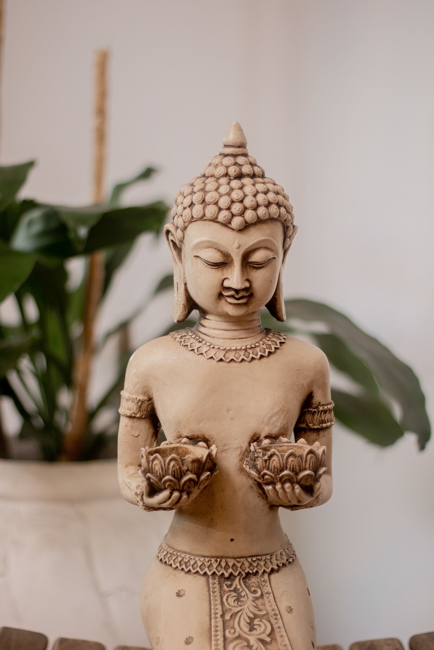 A statue of a seated figure with intricate patterns on the head and hands, set against a backdrop of greenery.