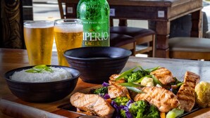 A dining table with a meal, including grilled fish and vegetables, and two glasses of beer. - Ilha Flat Hotel (Ilhabela)
