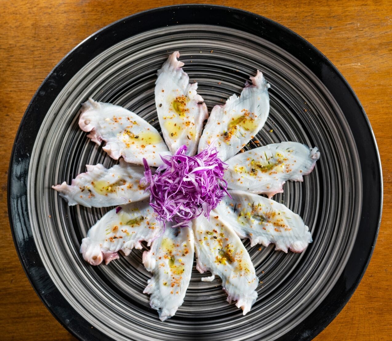 A black and white striped plate with octopus tentacles arranged in a flower-like pattern, garnished with purple cabbage and spices.