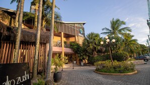 A building with a sign for 'Daiko Sushi Bar' and a paved area with palm trees and potted plants. - Ilha Flat Hotel (Ilhabela)