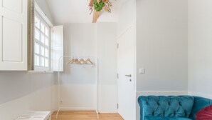 Une pièce avec un plancher en bois, un canapé bleu, un radiateur blanc et une porte ornée d’une plante suspendue.