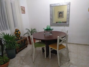 Un coin repas avec une table ronde, quatre chaises, une plante en pot, une statuette de hibou décorative et un miroir au mur.