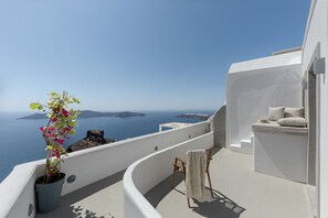 A balcony with a potted plant, a chair, and a view of the sea and islands. - Kaleidoscope Imerovigli Suites (Santorini)