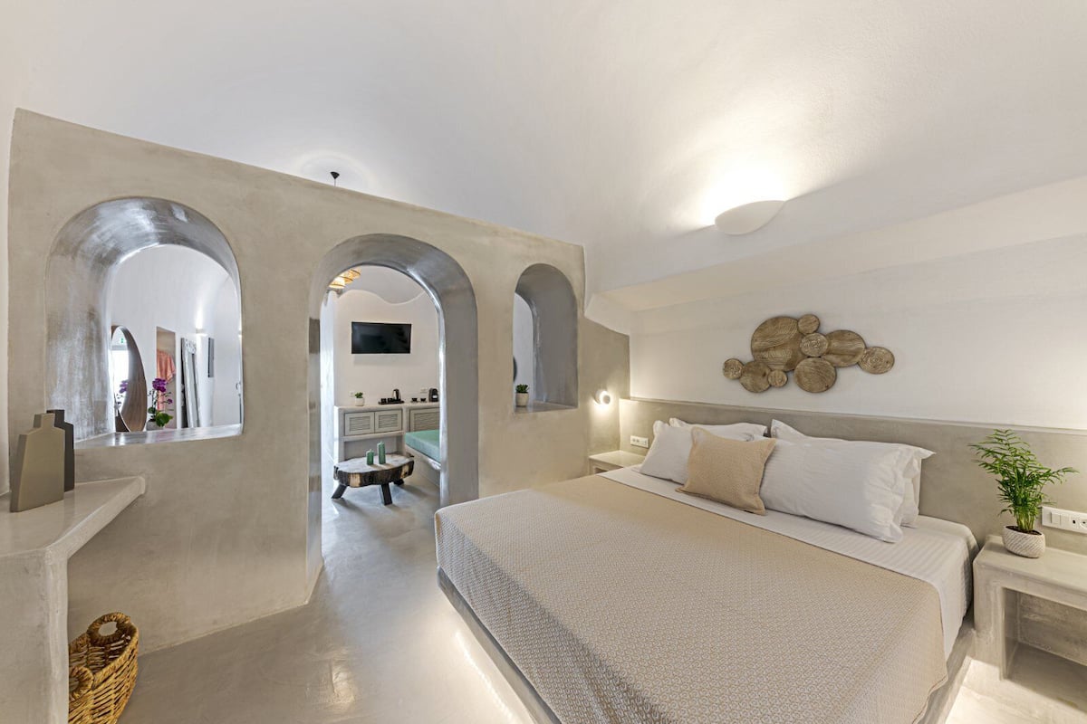 Une chambre à coucher moderne avec un grand lit, une coiffeuse et une salle de bain visible à travers une arche.