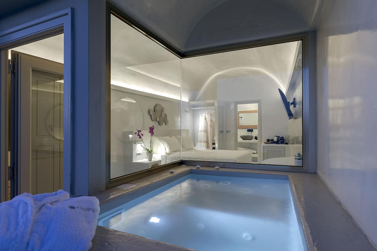 Une salle de bain moderne dotée d’un jacuzzi entouré de parois de verre, d’une zone de douche ouverte et d’un grand miroir qui reflète l’ensemble de la pièce.