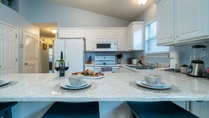 A kitchen with white cabinets, a marble countertop, and a central island with stools. - Panama City Beach Getaway | Games | Sleeps 8 |Pets (Panama City Beach)