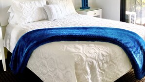 Habitación de hotel con cama, un cuadro de una ola, unidad de aire acondicionado, lámpara y ventana con vista a palmeras.