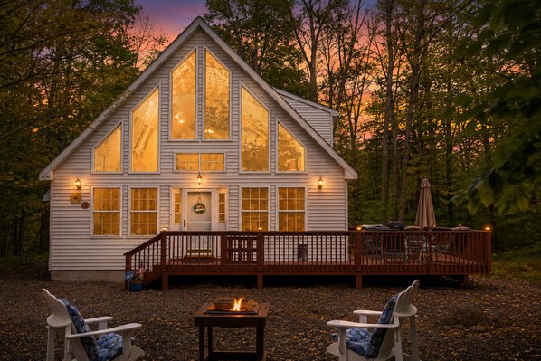 A cabin with large windows, a deck, and a fire pit.