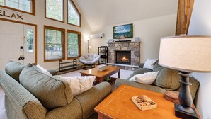 A cozy living room with a fireplace, large windows, and a comfortable seating area. - Chalet w/ firepit, deck, BBQ, fireplace, Wi-Fi, AC, close to waterparks, skiing (Pocono Lake)