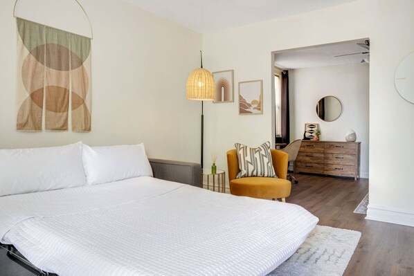 A bedroom with a large bed, a chair, a dresser, and a lamp.