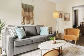 A modern living room with a grey sofa, a round coffee table, a tall floor lamp, and a small plant.