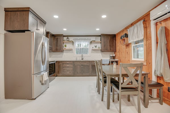 Une cuisine moderne avec des meubles en bois, un réfrigérateur en acier inoxydable et un coin repas comprenant une table et des chaises en bois.