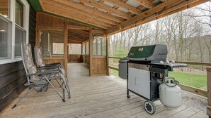 Un espacio al aire libre techado con una parrilla, tanque de gas, cubierta de madera y una silla.
