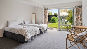 A hotel room with two beds, a small table, and a chair. There is a sliding glass door leading to an outdoor area with a garden and a table. - Henry`s Bach with Wi-Fi, private rear garden for alfesco dining (Taupō)