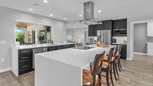 A modern kitchen with a large island, dark cabinetry, stainless steel appliances, and a view of the outdoors. - Seven Palms Waterfront - Private Dock, Heated Pool & Lanai - Walk to Beach! (West Palm Beach)