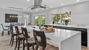A modern kitchen with a large island, built-in appliances, and large windows offering views of greenery. - Seven Palms Waterfront - Private Dock, Heated Pool & Lanai - Walk to Beach! (West Palm Beach)