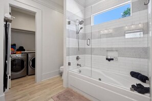Ein modernes Badezimmer mit einer gläsernen Duschkabine, einer weißen Badewanne und einer Waschküche mit zwei Waschmaschinen.