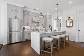 Une cuisine moderne avec des meubles blancs, un Ăźlot en marbre et des luminaires suspendus.