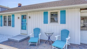 Ein Haus mit Veranda, zwei blaue Adirondack-Stühle, ein kleiner runder Tisch und eine Tür mit blauen Fensterläden.