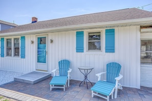 A house with a porch, two blue Adirondack chairs, a small round table, and a door with blue shutters. - "STEPS TO SAND - Two Cottage Classic Gem Retreat" (Milton)