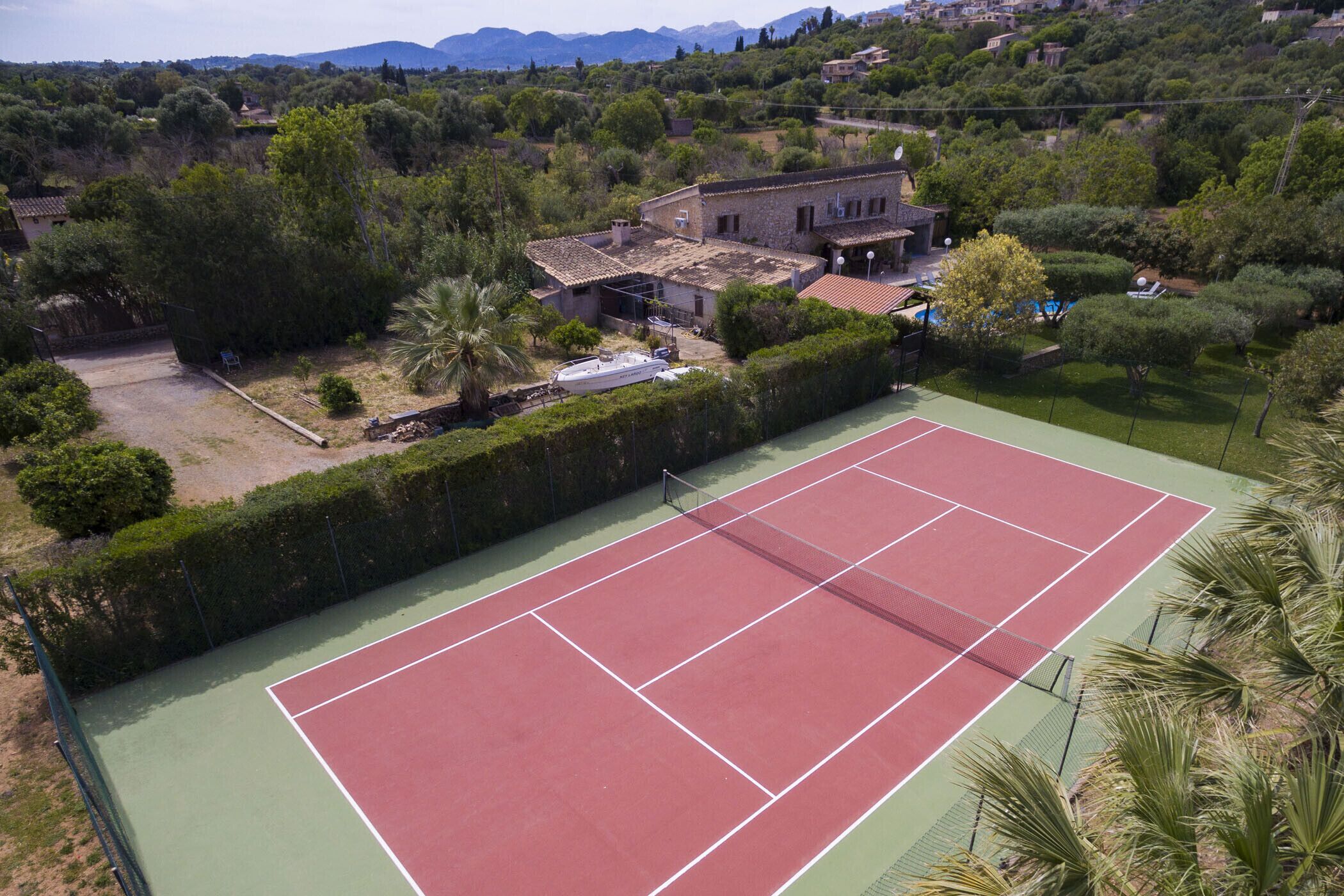 A tennis court surrounded by a lush garden and a stone building.