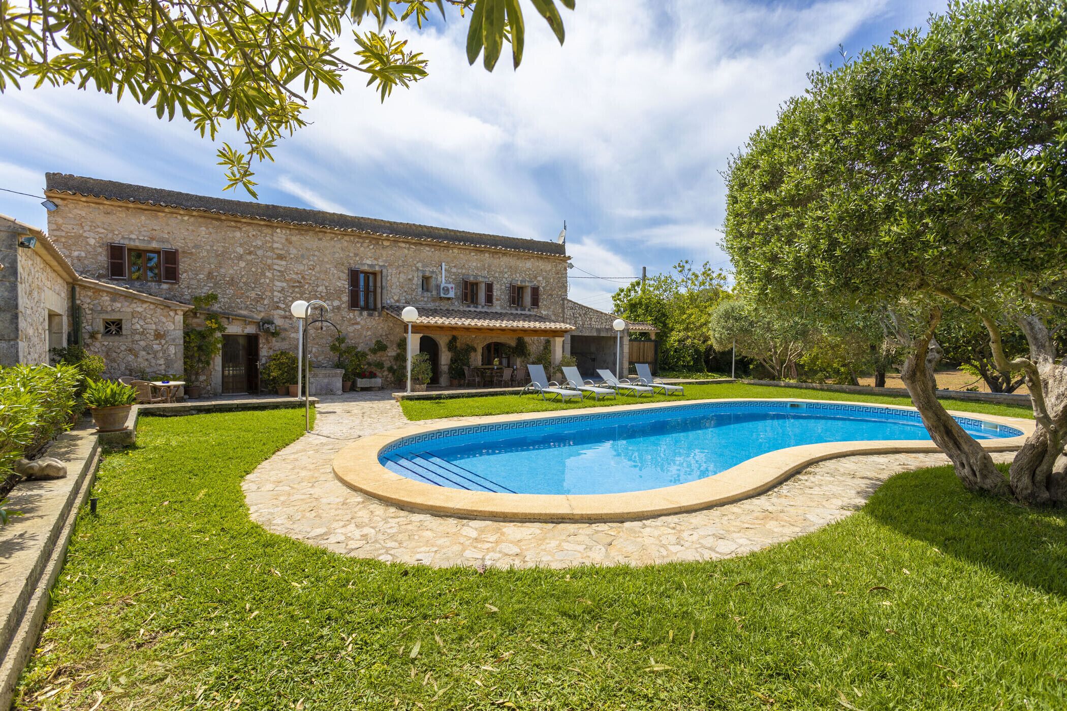 Une villa en pierre dotée d’une piscine, entourée d’une pelouse bien entretenue et d’arbres.