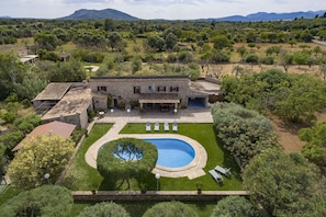 A villa with a swimming pool, surrounded by lush greenery and mountains in the background.