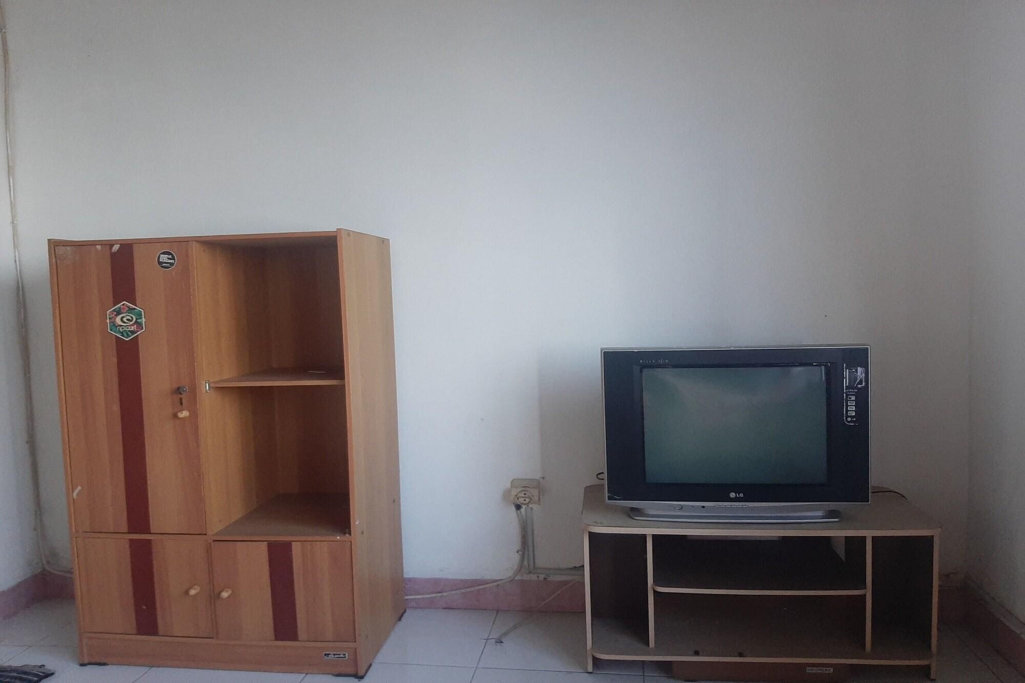 A wooden cabinet with a logo, a television on a stand, and a wall socket.