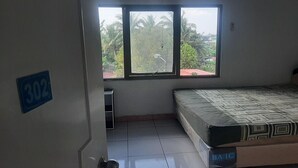 Una habitación con una cama, un ventanal con vistas a palmeras y una puerta con un letrero de número.