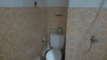 A bathroom with patterned tiles, a toilet, a shower, and a small shelf with a bottle.