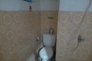 A bathroom with patterned tiles, a toilet, a shower, and a small shelf with a bottle.
