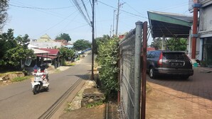 Una calle con un coche estacionado y una motocicleta, edificios con techos rojos, y líneas eléctricas aéreas.