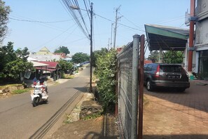 Una calle con un coche estacionado y una motocicleta, edificios con techos rojos, y líneas eléctricas aéreas.