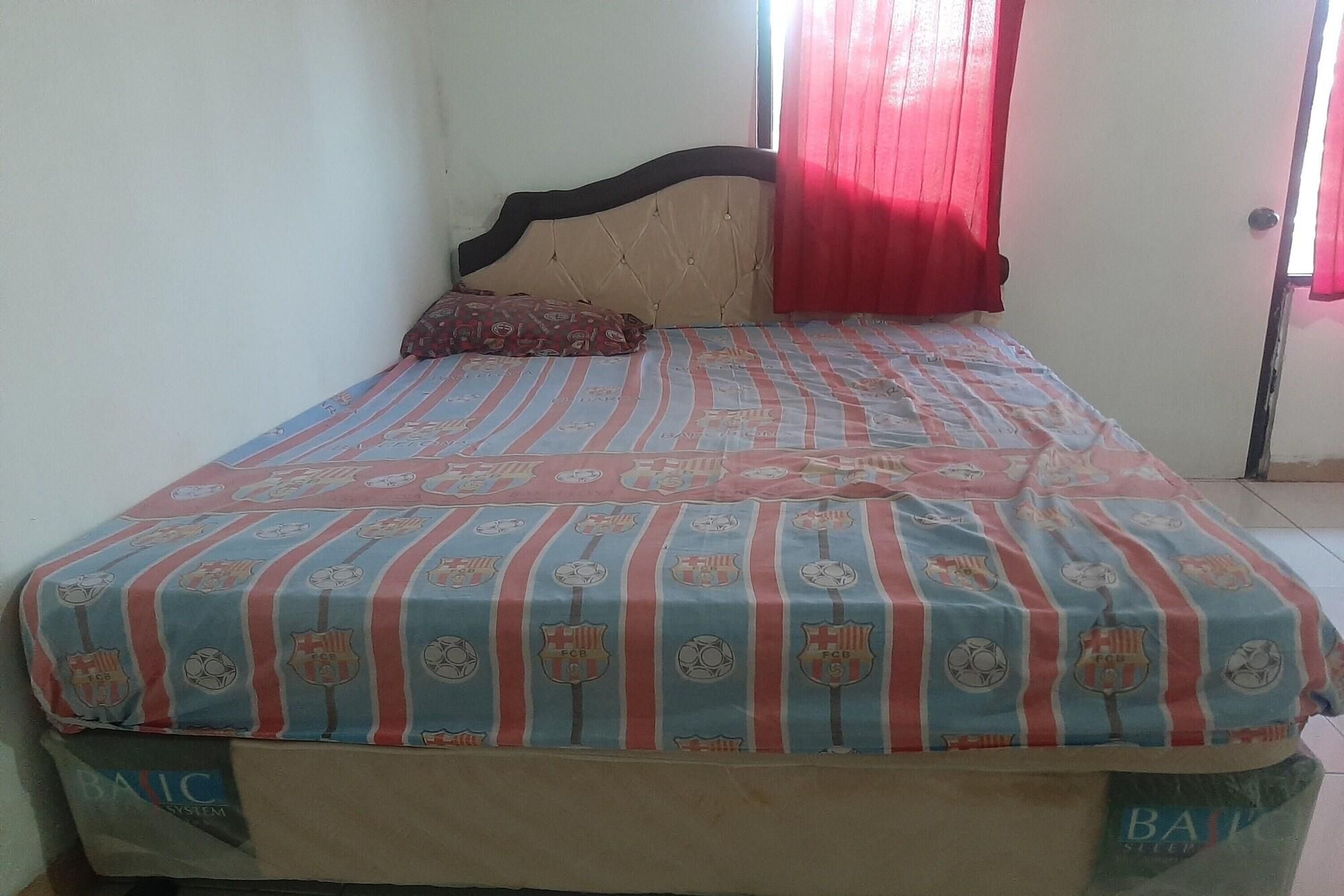 A bed with a striped bedspread, a headboard, a pillow, and a window with red curtains.
