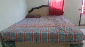 A bed with a striped bedspread, a headboard, a pillow, and a window with red curtains.