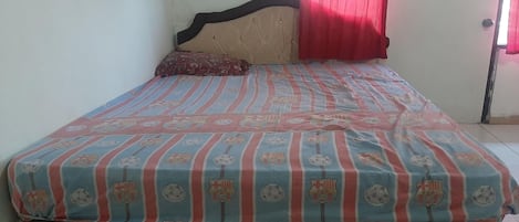 A bed with a striped bedspread, a headboard, a pillow, and a window with red curtains.
